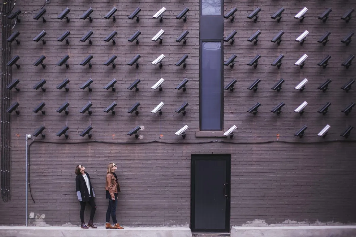 Two people looking up at a wall covered in surveillance cameras
